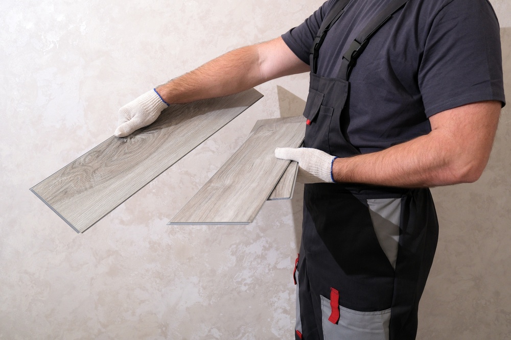 Instalador sosteniendo piezas de piso SPC tipo madera para instalación interior.