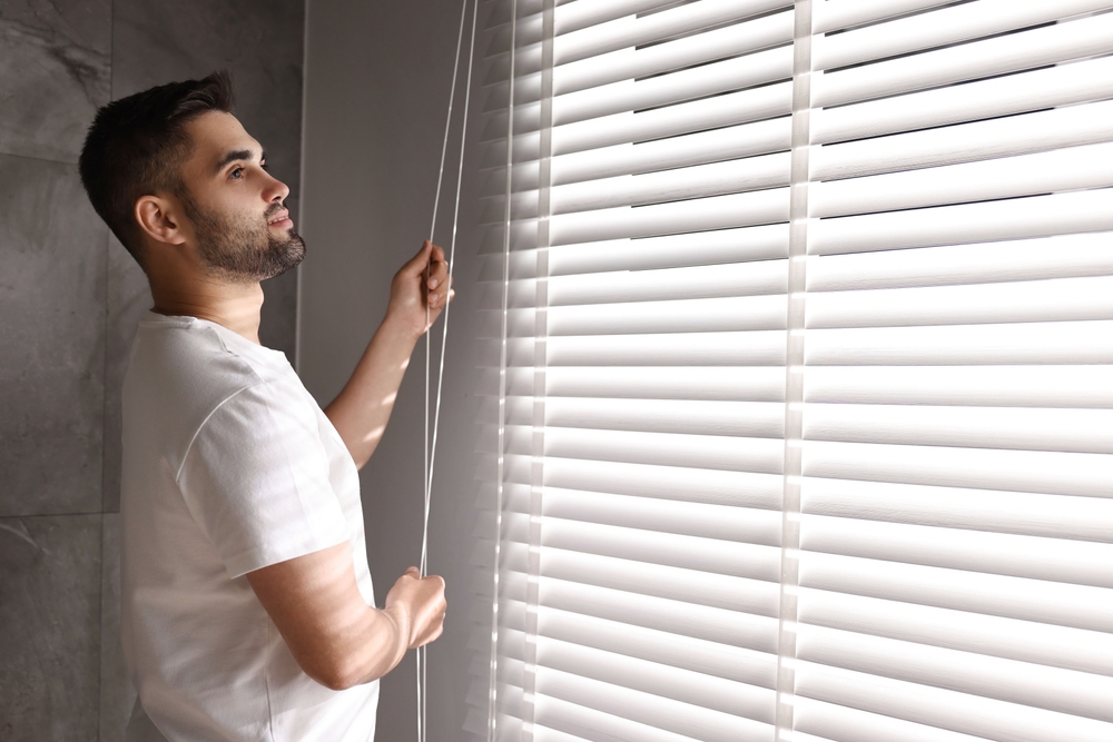 Hombre ajustando persianas blancas de Terza, ejemplo de diseño moderno y funcional para el control de luz en interiores.